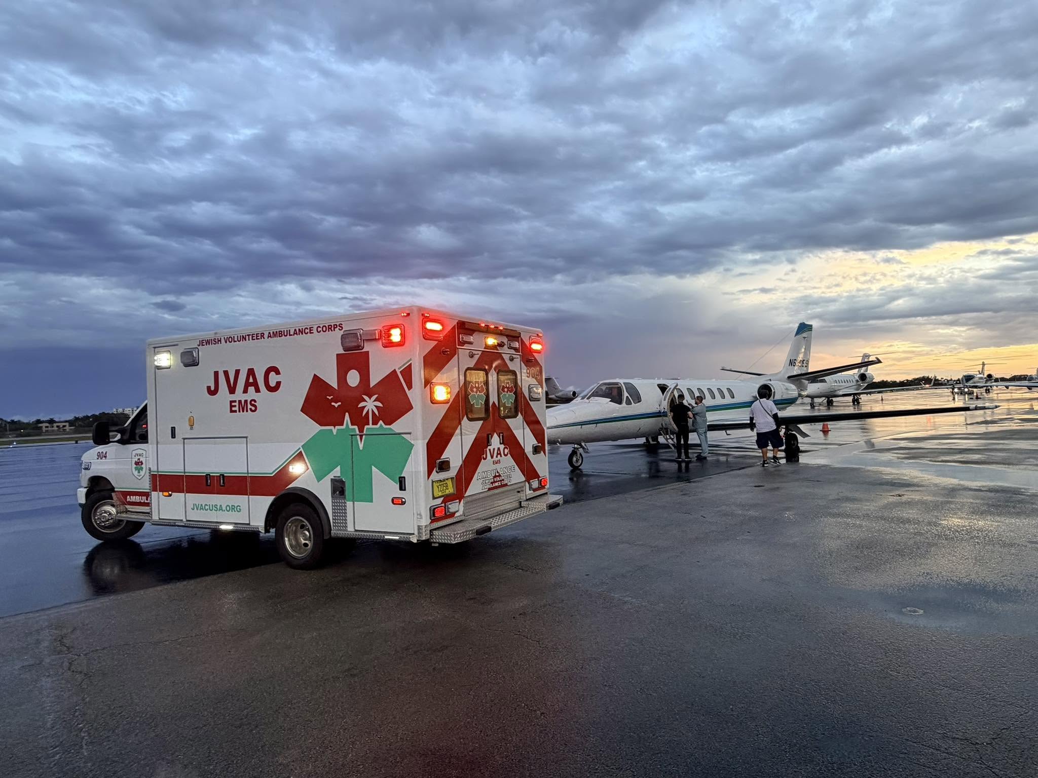 JVAC ambulance beside an aircraft on a wet airfield at sunset